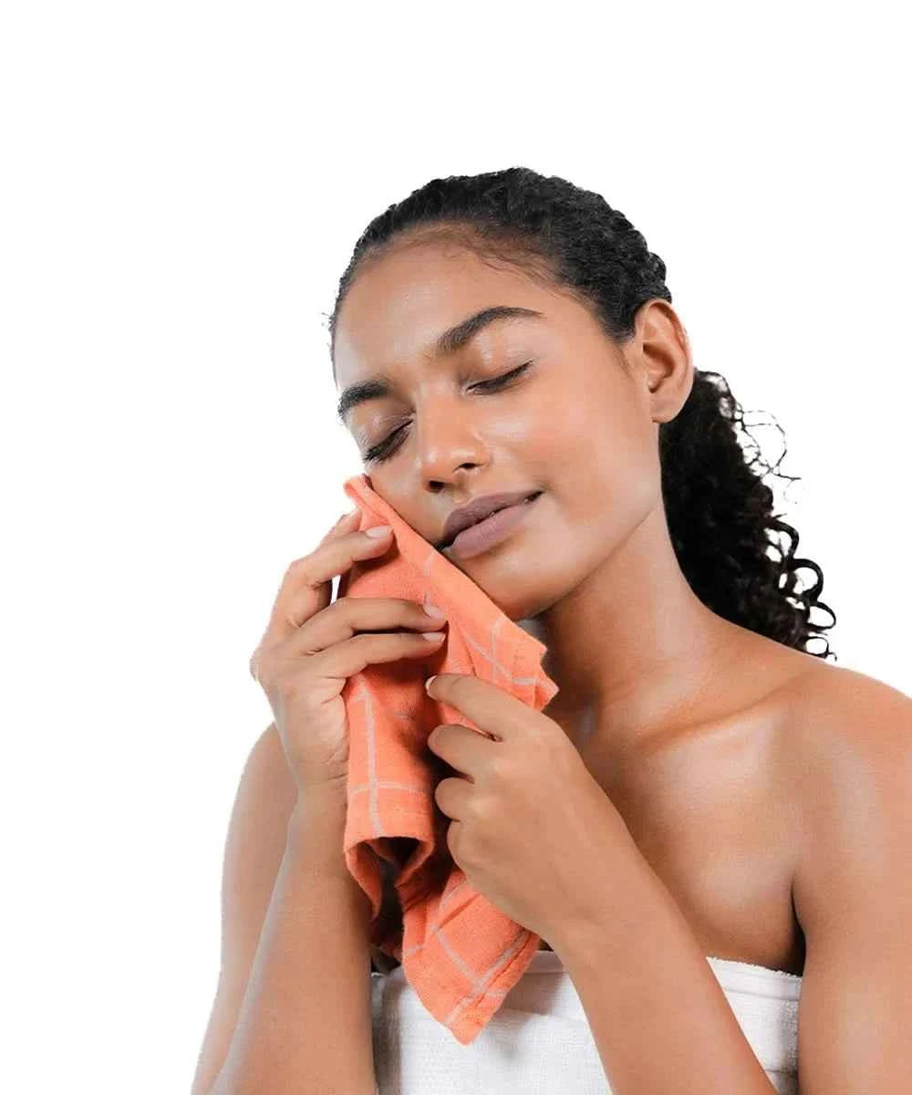 Woman cleaning her face with an orange towel on a white background